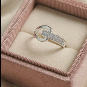 silver ring with a unique belt buckle design and embedded zircon stones, displayed in a blush pink velvet ring box on satin fabric.