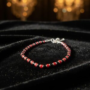 Handcrafted red, black, and white beaded bracelet worn on wrist in natural sunlight, with coffee and book in background — minimalist unisex accessory for protection and style.