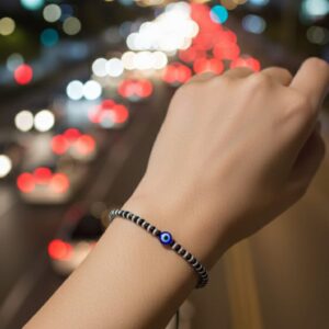 Black beaded bracelet with a central blue evil eye charm, laid on a black velvet background — minimalist unisex accessory symbolizing spiritual protection and grounding.